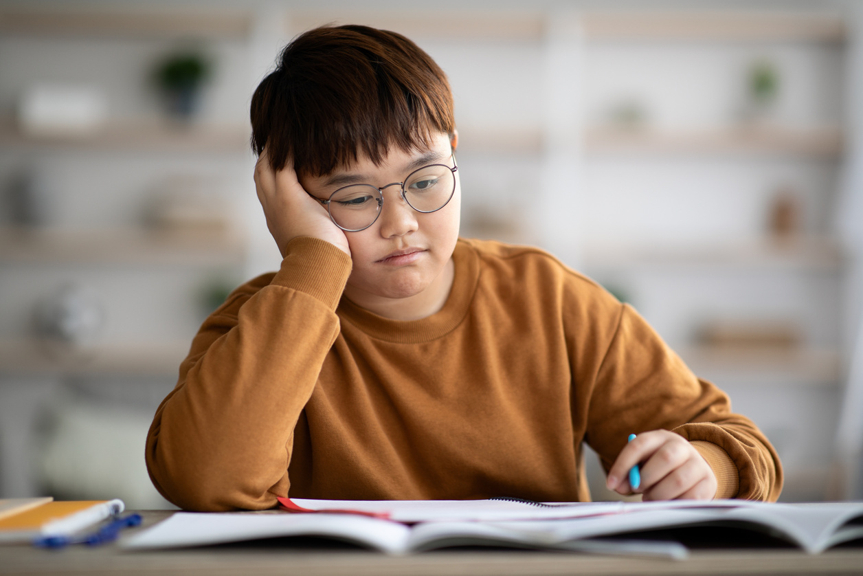 Bored schooler doing homework, leaning on his hand